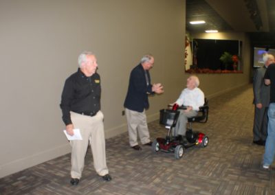 Three men standing in a hallway with one man sitting on a scooter.