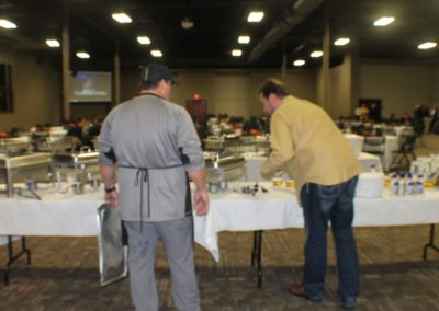 Two men standing at a table with plates of food.
