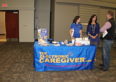 Two people standing next to a table with an electronic caregiver sign.