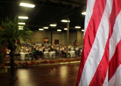 A large room with people sitting at tables and an american flag.